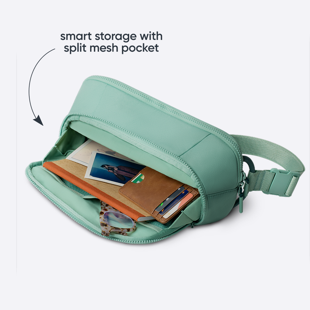 All-Day Crossbody in Sea Glass, sage green ripstop body unzipped to show internal split mesh pocket holding cards, a wallet, and a phone, with text reading "smart storage with split mesh pocket"