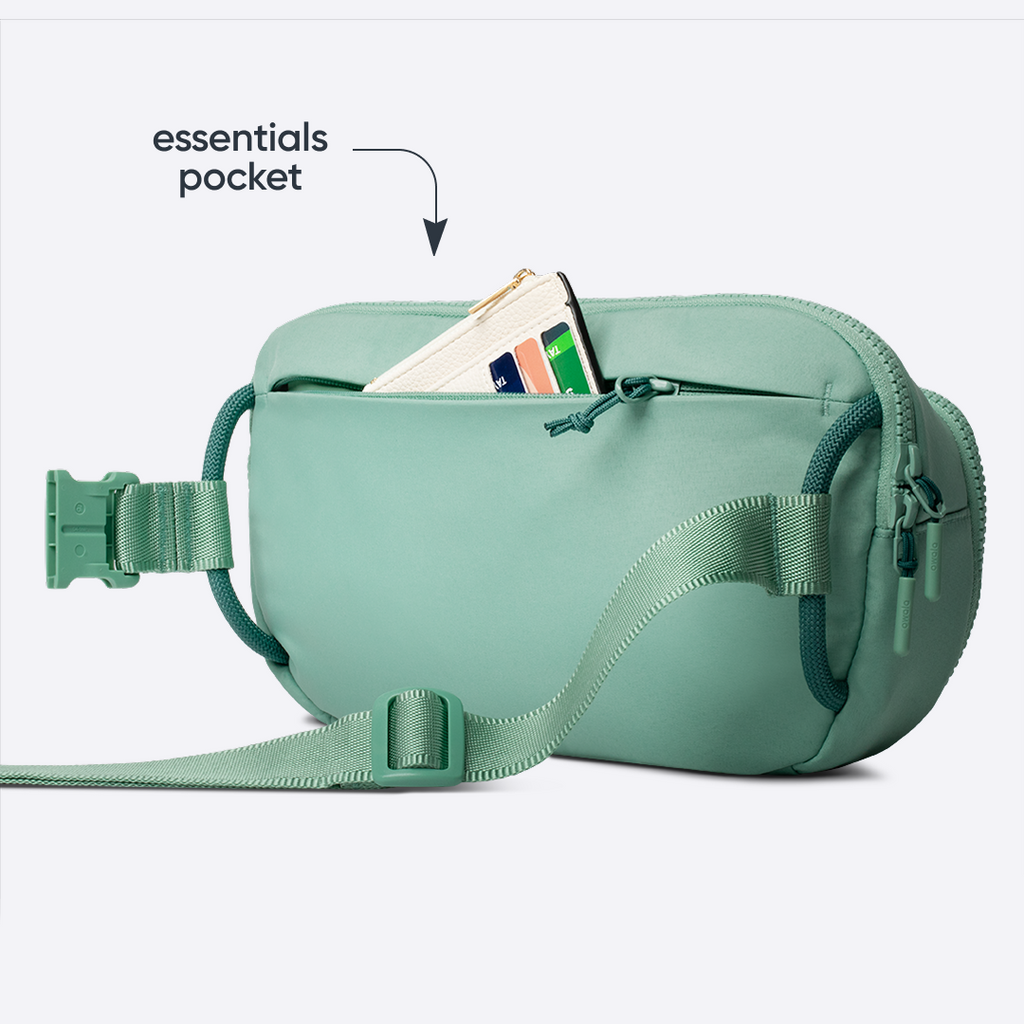 All-Day Crossbody in Sea Glass, sage mint belt bag with matching strap and front zip pocket holding a card, with text reading "essentials pocket" pointing to the open pocket